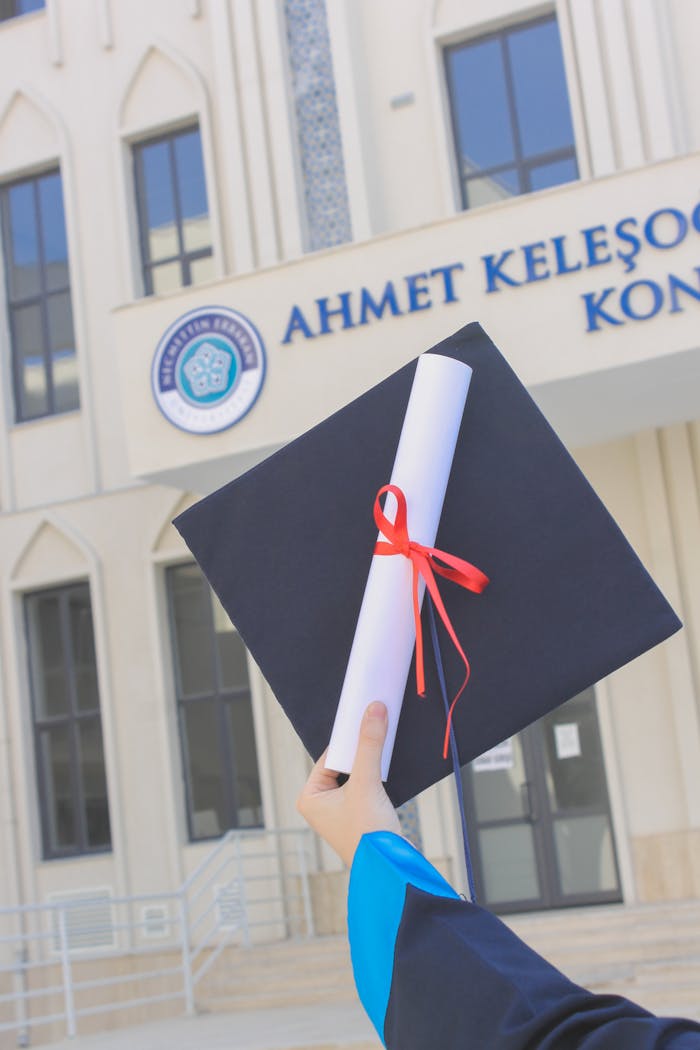 Close-up of a graduation cap and diploma held outdoors in front of a building.