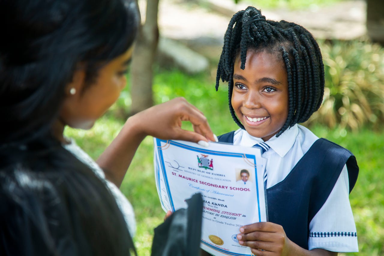 A smiling young girl receives a certificate outdoors at St. Maurice Secondary School.