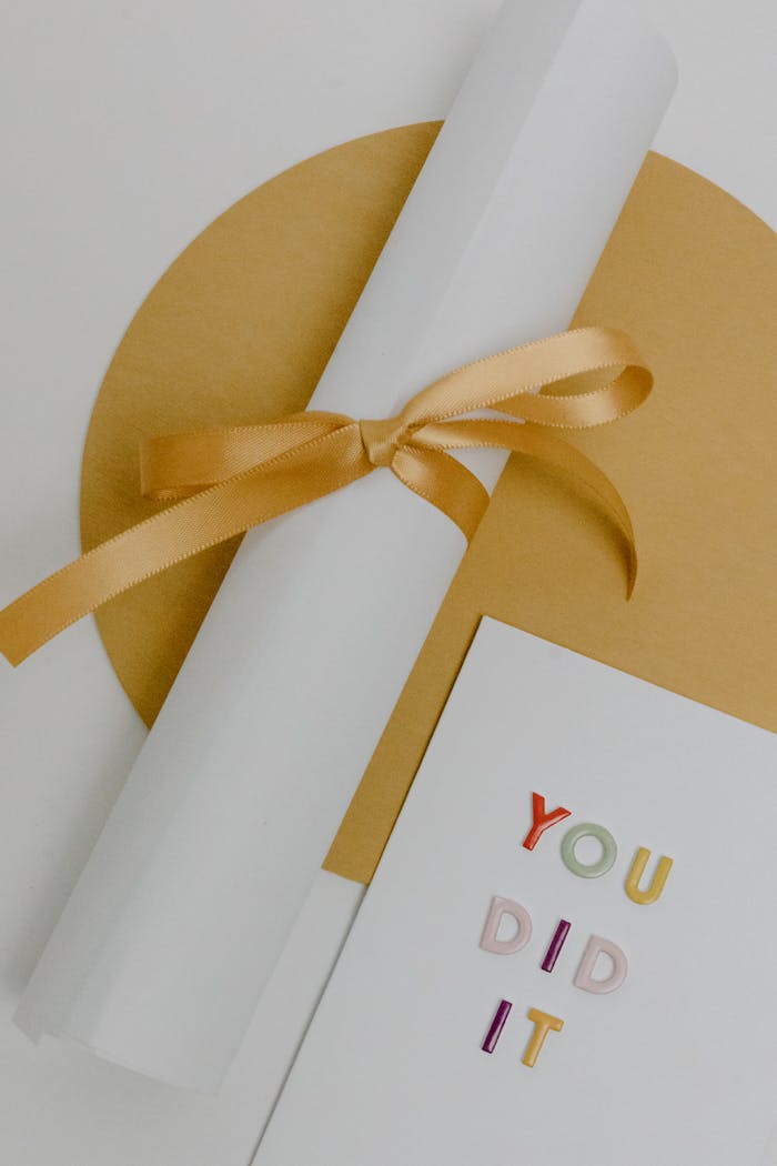 Rolled white certificate tied with gold ribbon on textured background next to congratulatory card.